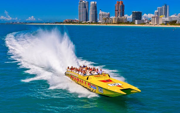 Speedboat with tourists on Miami sightseeing tour, city skyline in background.