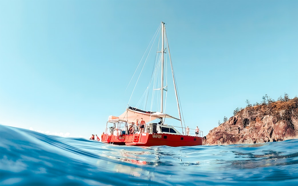 Catamaran sailing near rocky shore in Whitsundays, Australia.