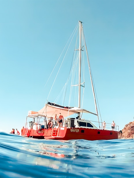 Catamaran sailing near rocky shore in Whitsundays, Australia.