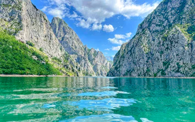 Komani Lake surrounded by steep rocky cliffs under a blue sky.