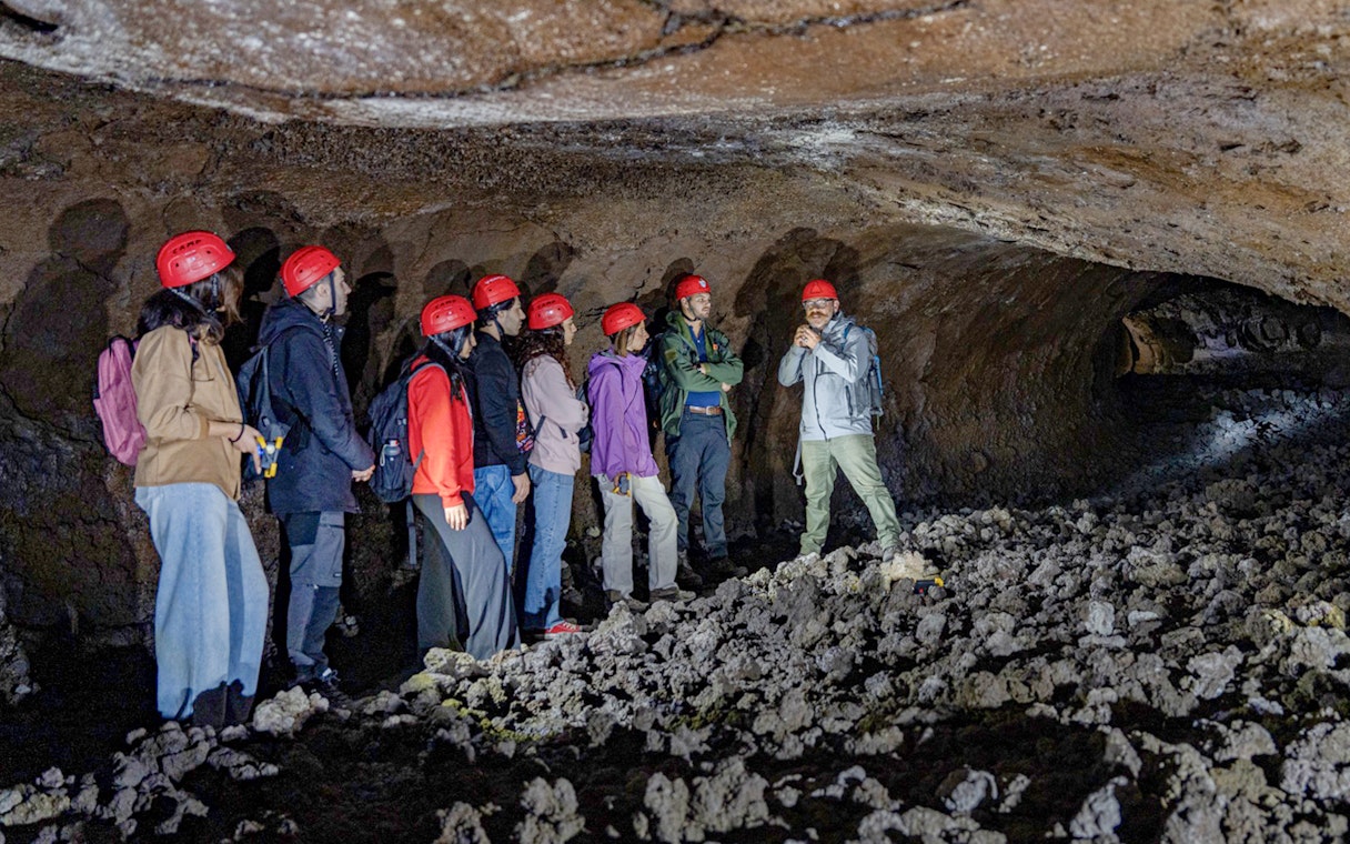 Tour group exploring lava caves near Mount Etna with a guide.