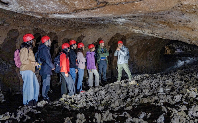 Tour group exploring lava caves near Mount Etna with a guide.