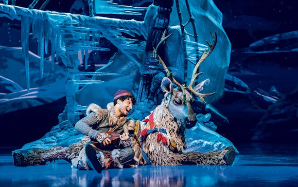 Man playing guitar next to reindeer on stage in Disney's Die Eiskönigin show.