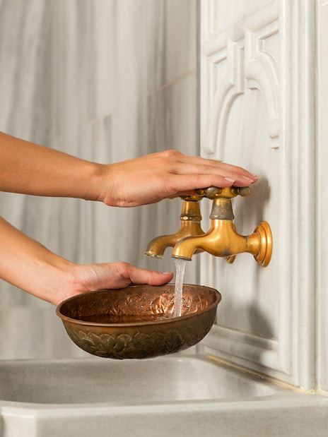 Hands filling a bowl from brass taps in a historical hammam in Cappadocia, Turkey.
