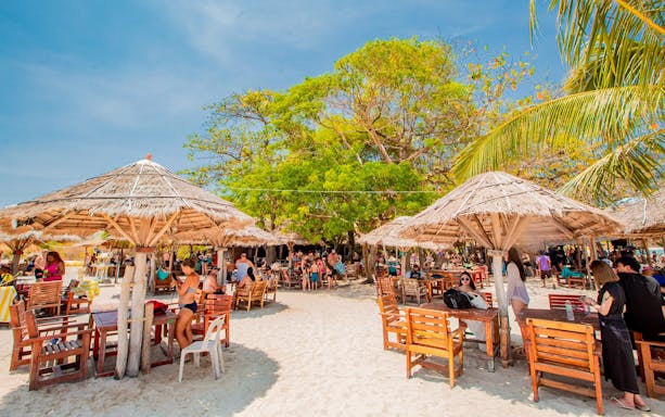 Beachside dining area with wooden tables and thatched umbrellas on Koh Samui Pig Island tour.