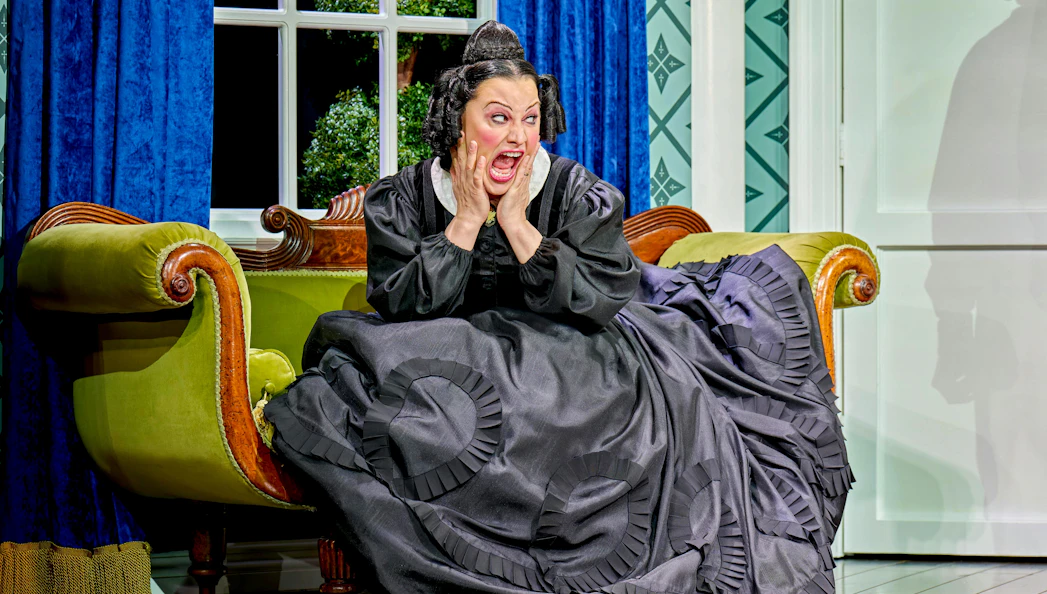 Woman in period costume on a vintage sofa, expressing surprise, from "Oh Mary!" show.