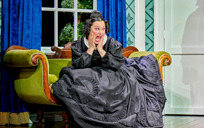 Woman in period costume on a vintage sofa, expressing surprise, from "Oh Mary!" show.