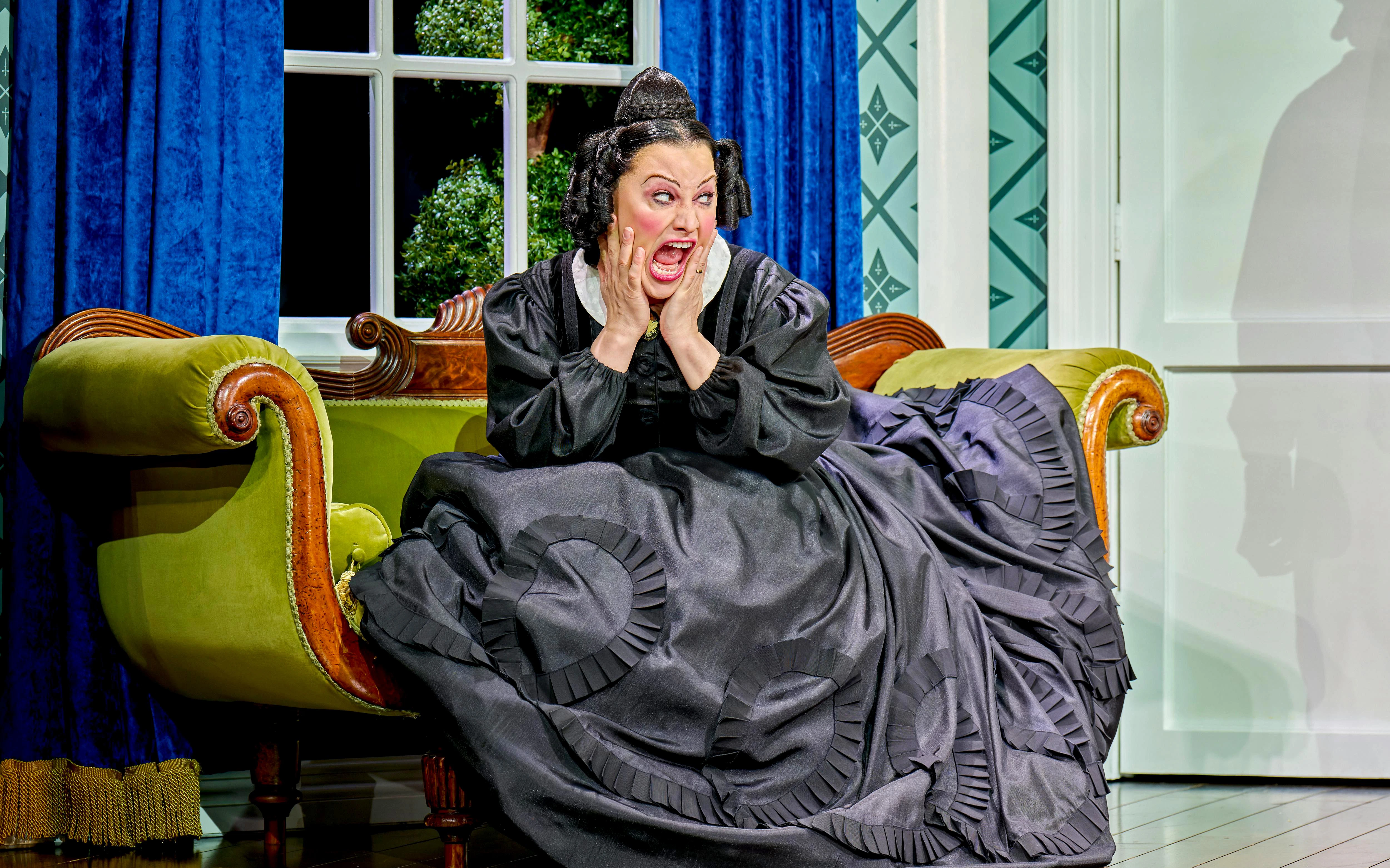 Woman in period costume on a vintage sofa, expressing surprise, from "Oh Mary!" show.