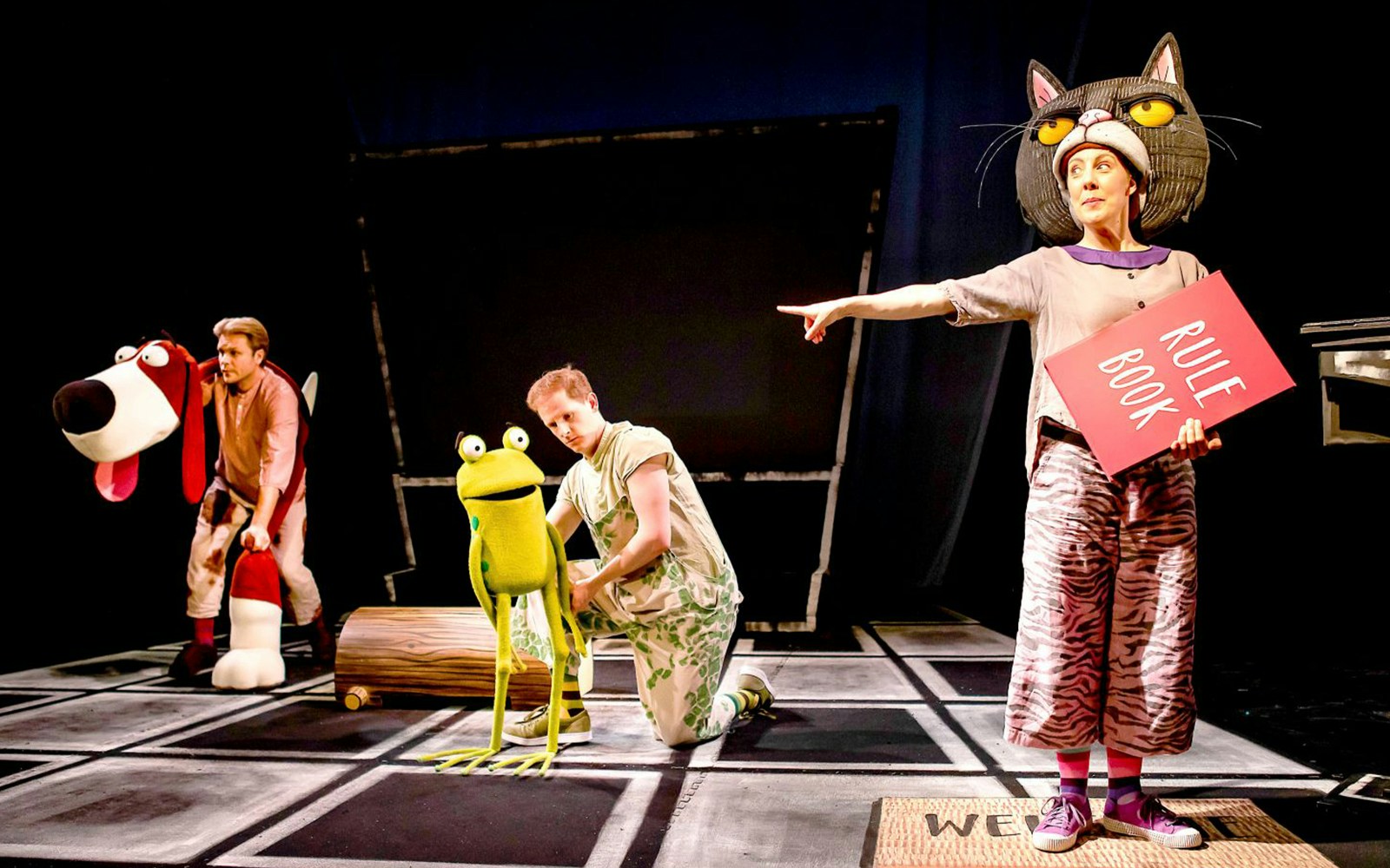Actors performing "Oi Frog & Friends!" with frog puppet and rule book.