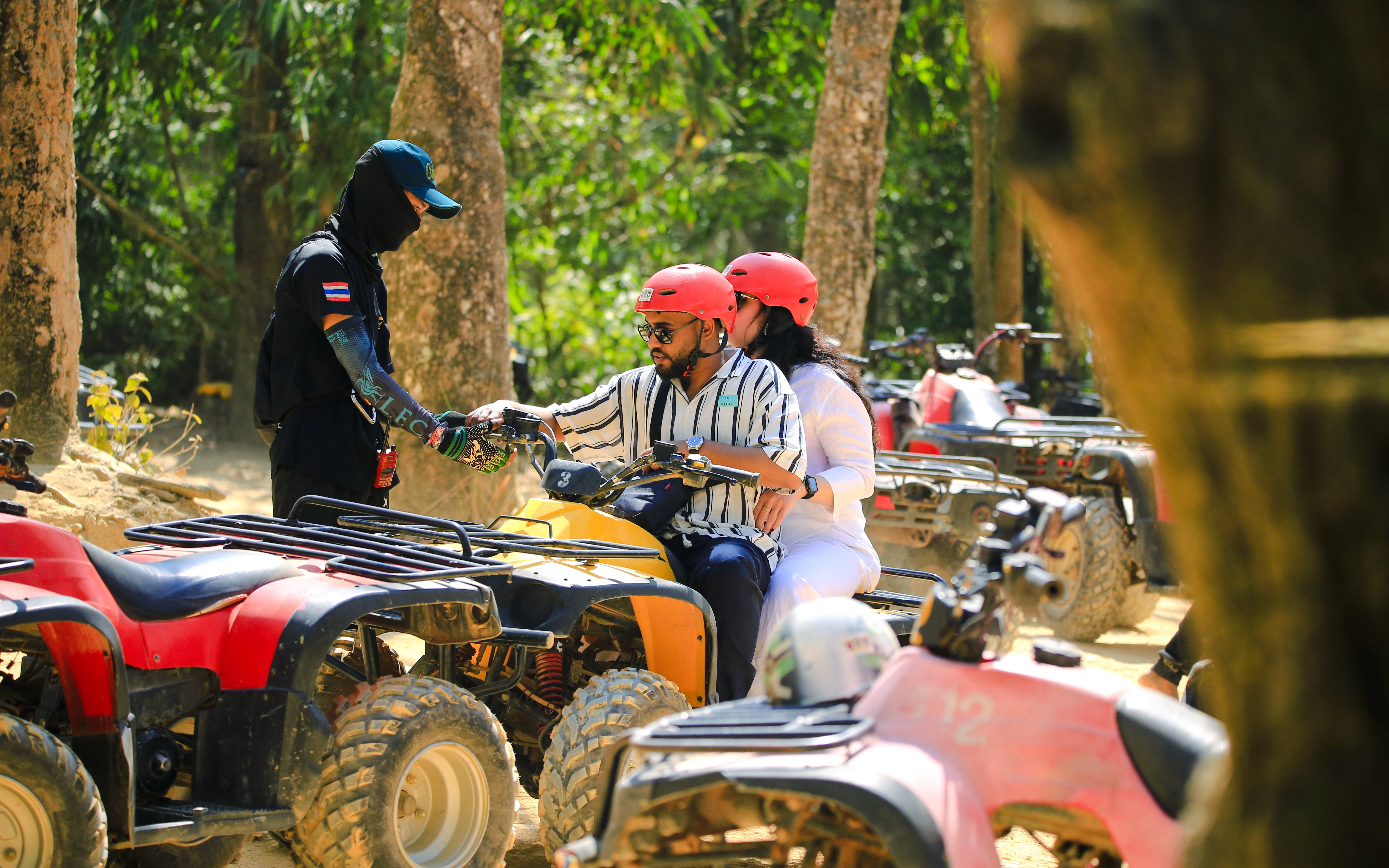 Couple on ATV receiving instructions from guide in forest setting.
