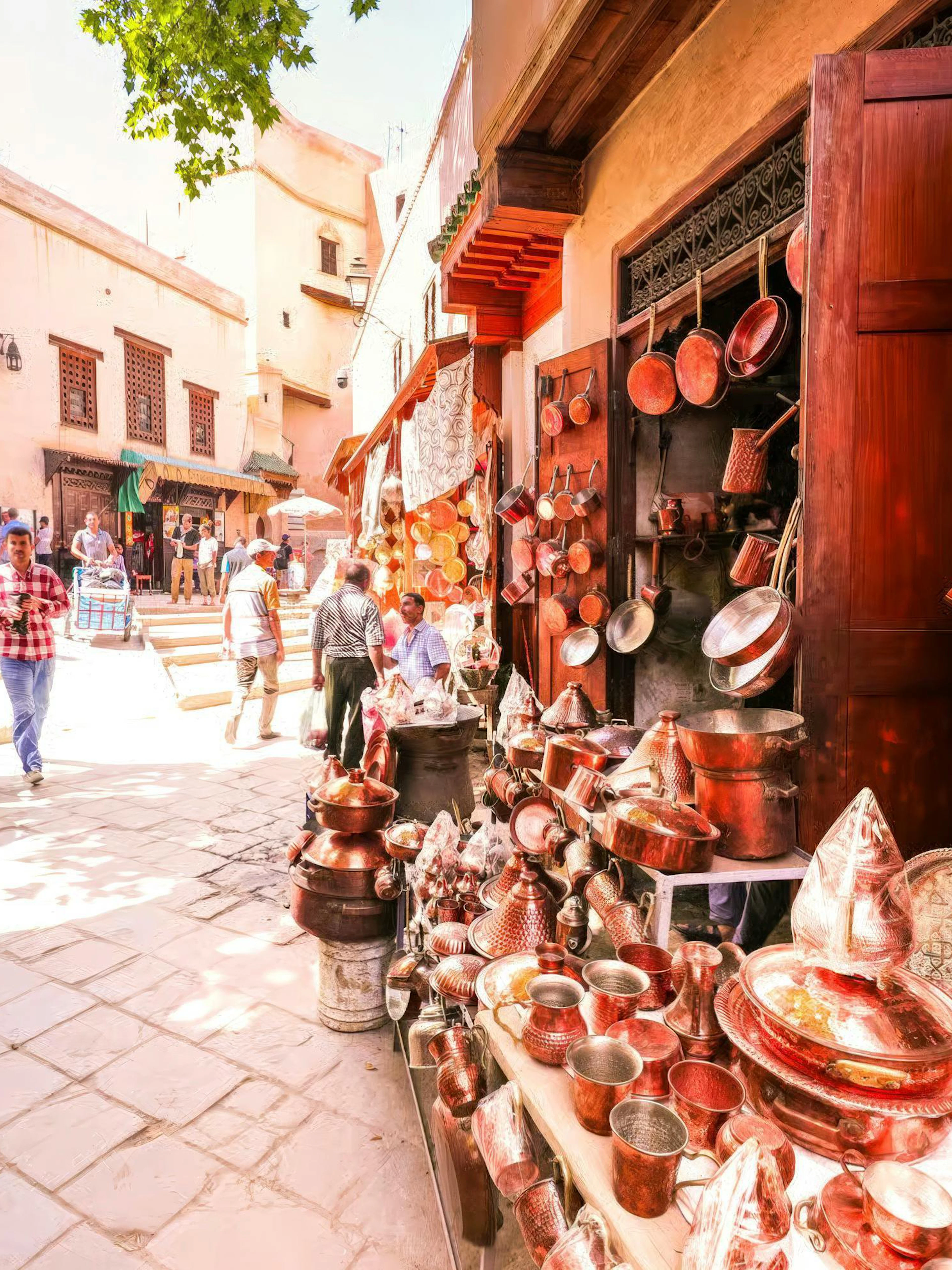 Copperware shop in Fes Medina with people walking near Al Attarine Madrasa entrance.
