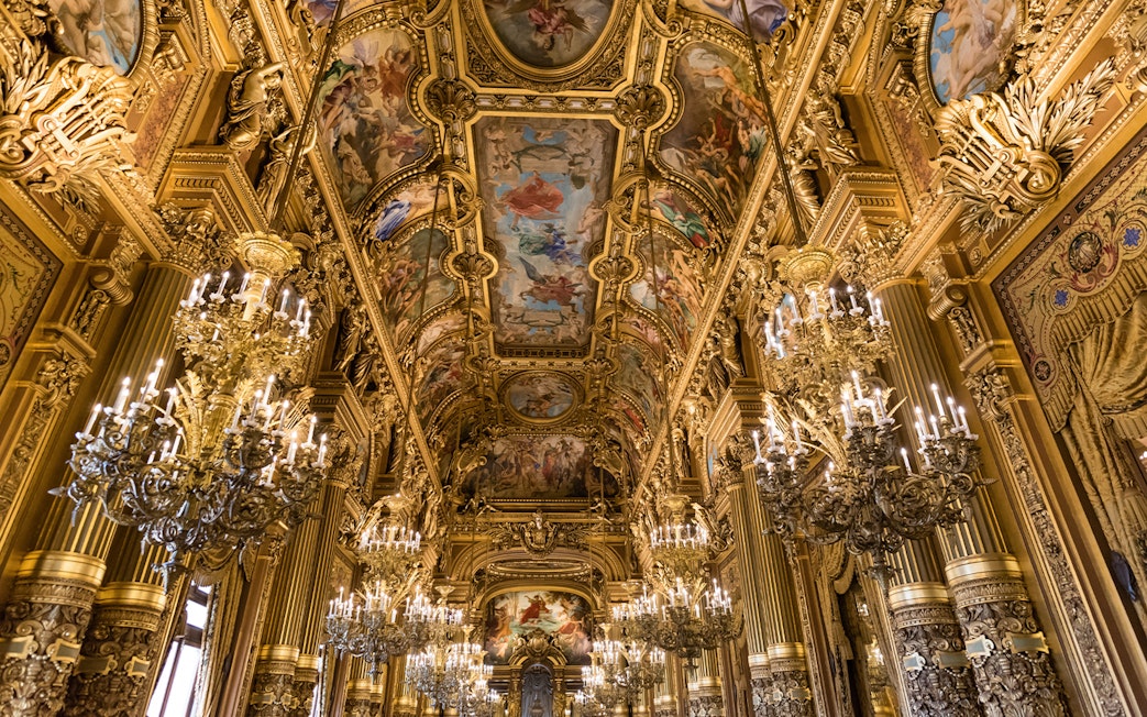Grand Foyer of Palais Garnier Opera with ornate chandeliers and detailed ceiling frescoes.
