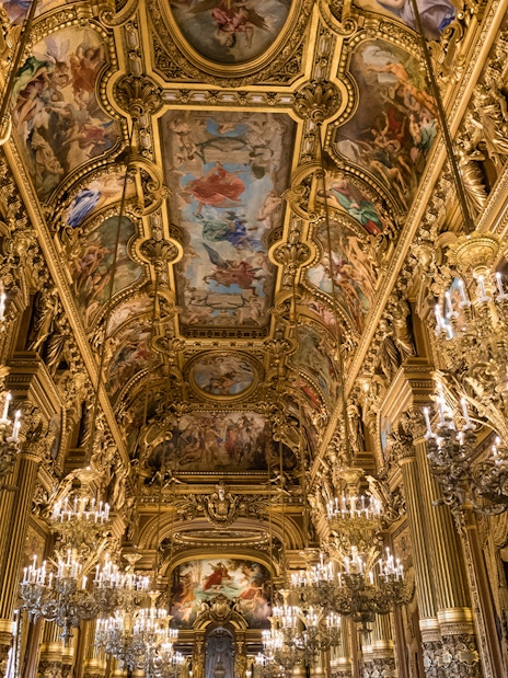 Grand Foyer of Palais Garnier Opera with ornate chandeliers and detailed ceiling frescoes.