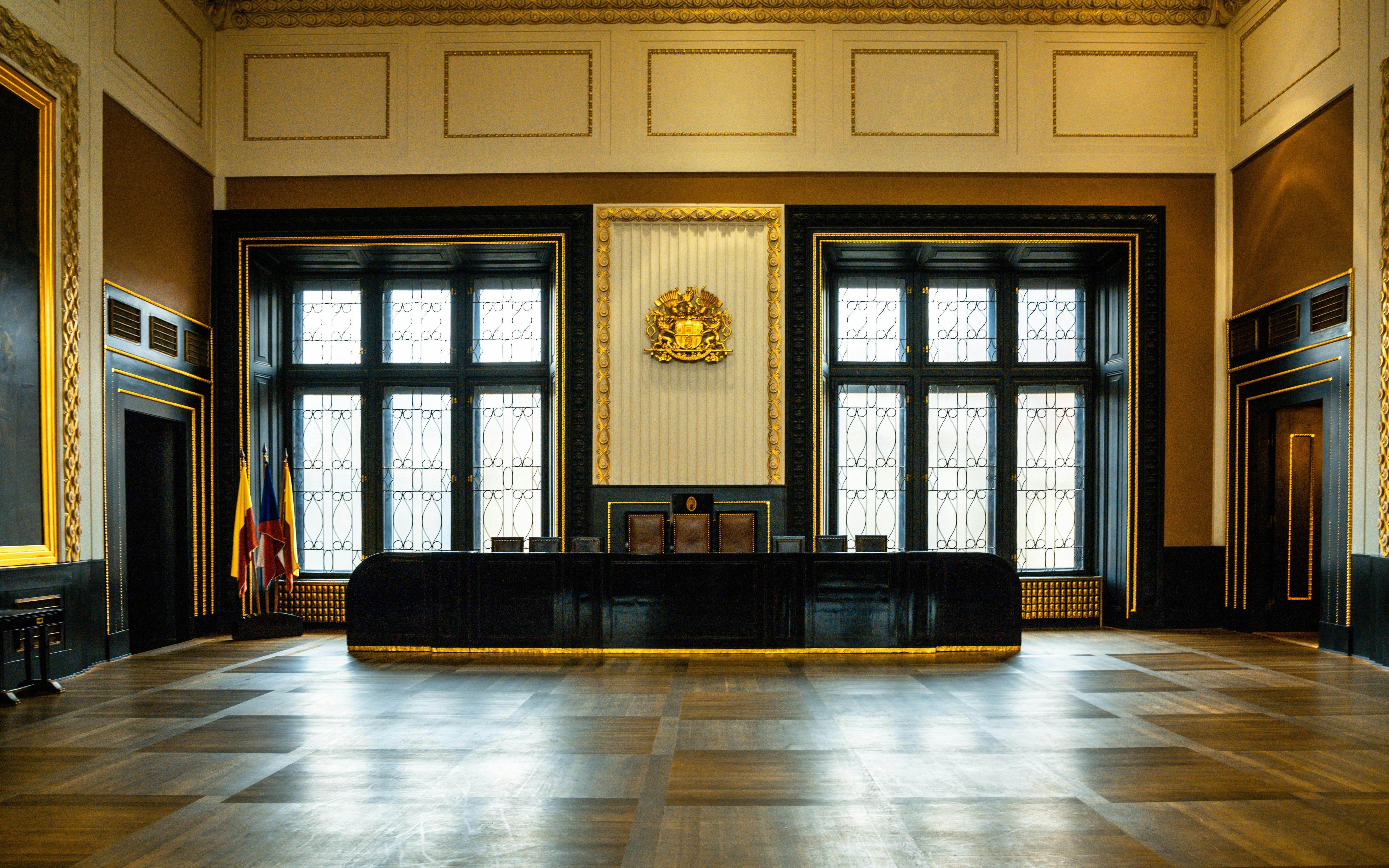 Interior of a historic hall with ornate windows and flags, Prague.