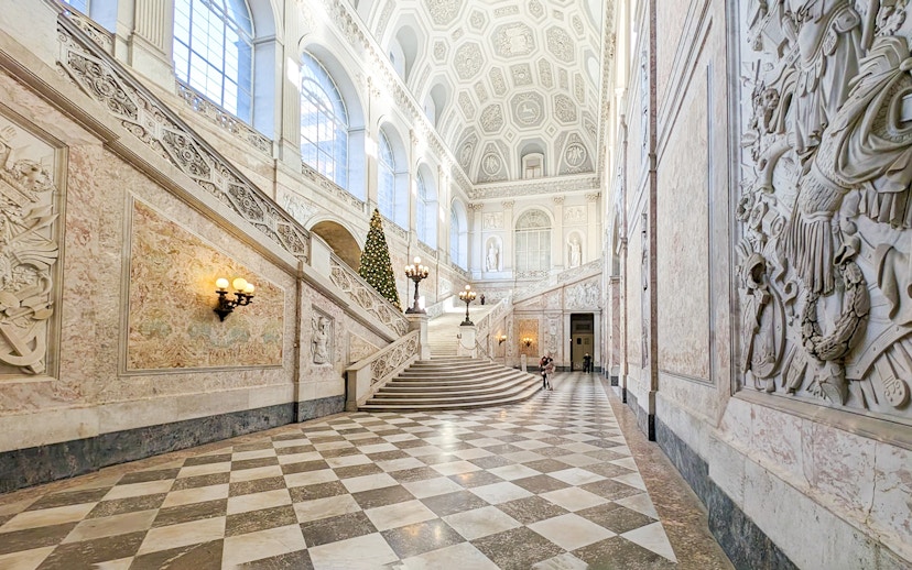 Grand staircase inside the Royal Palace of Naples with ornate decorations and a Christmas tree.