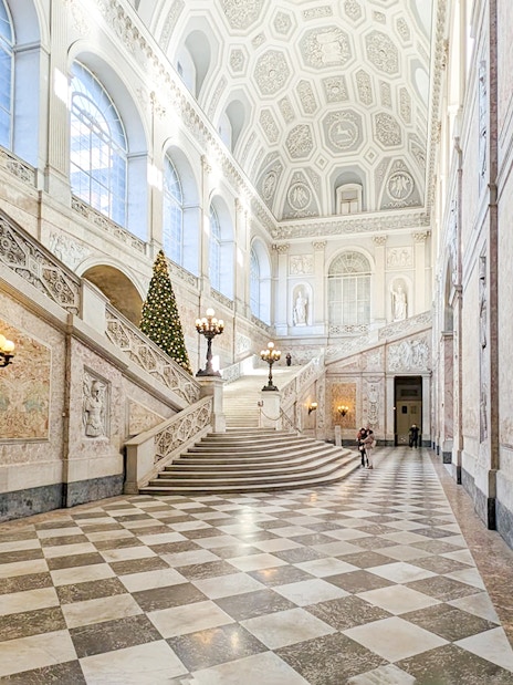 Grand staircase inside the Royal Palace of Naples with ornate decorations and a Christmas tree.