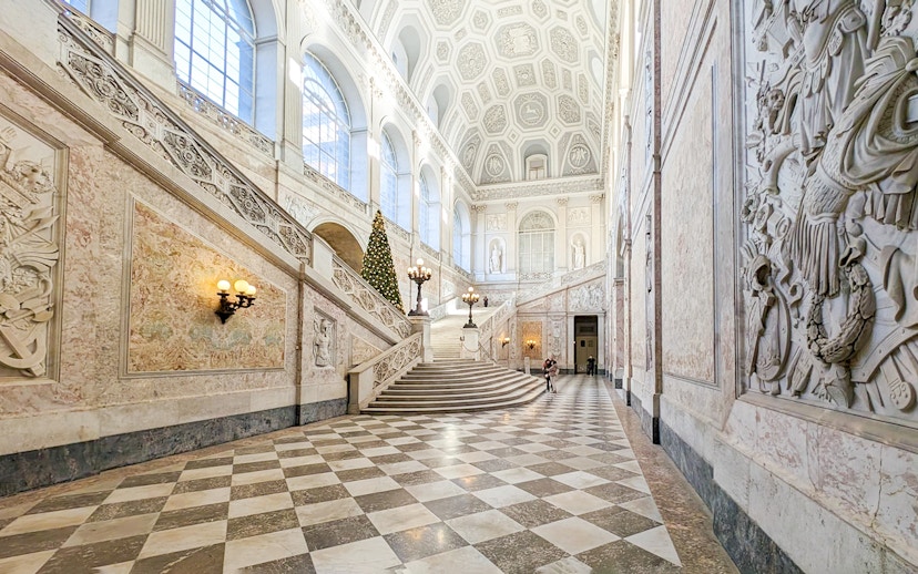 Grand staircase inside the Royal Palace of Naples with ornate decorations and a Christmas tree.
