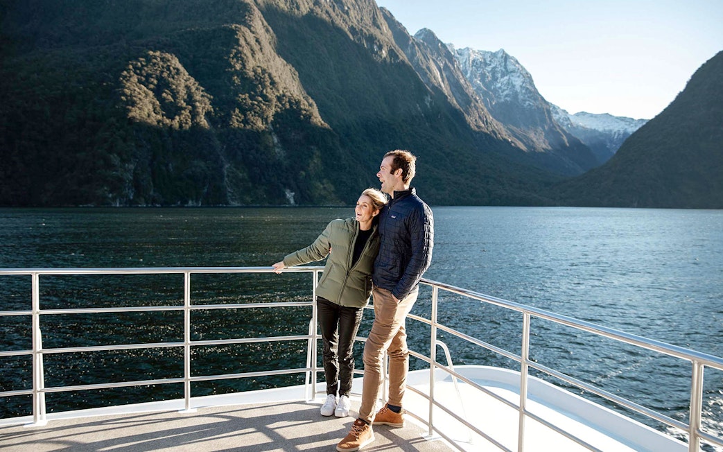 Couple on a boat enjoying Milford Sound's scenic mountain views.
