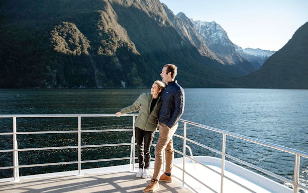 Couple on a boat enjoying Milford Sound's scenic mountain views.
