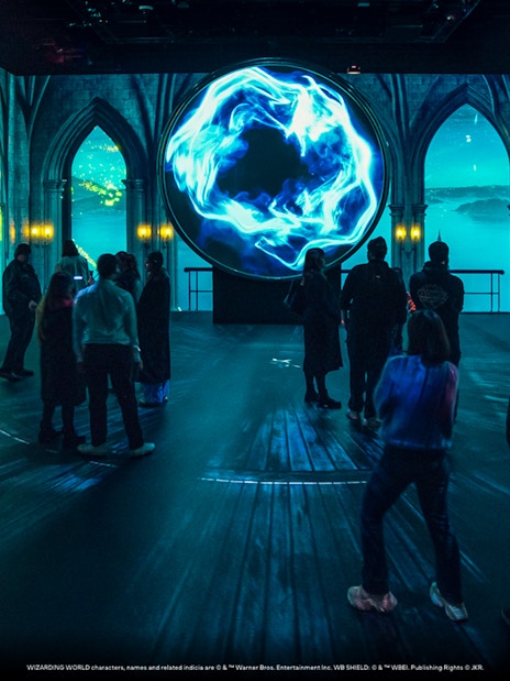 Visitors explore a magical exhibit with glowing blue orb at Harry Potter: Visions of Magic.