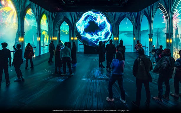 Visitors explore a magical exhibit with glowing blue orb at Harry Potter: Visions of Magic.