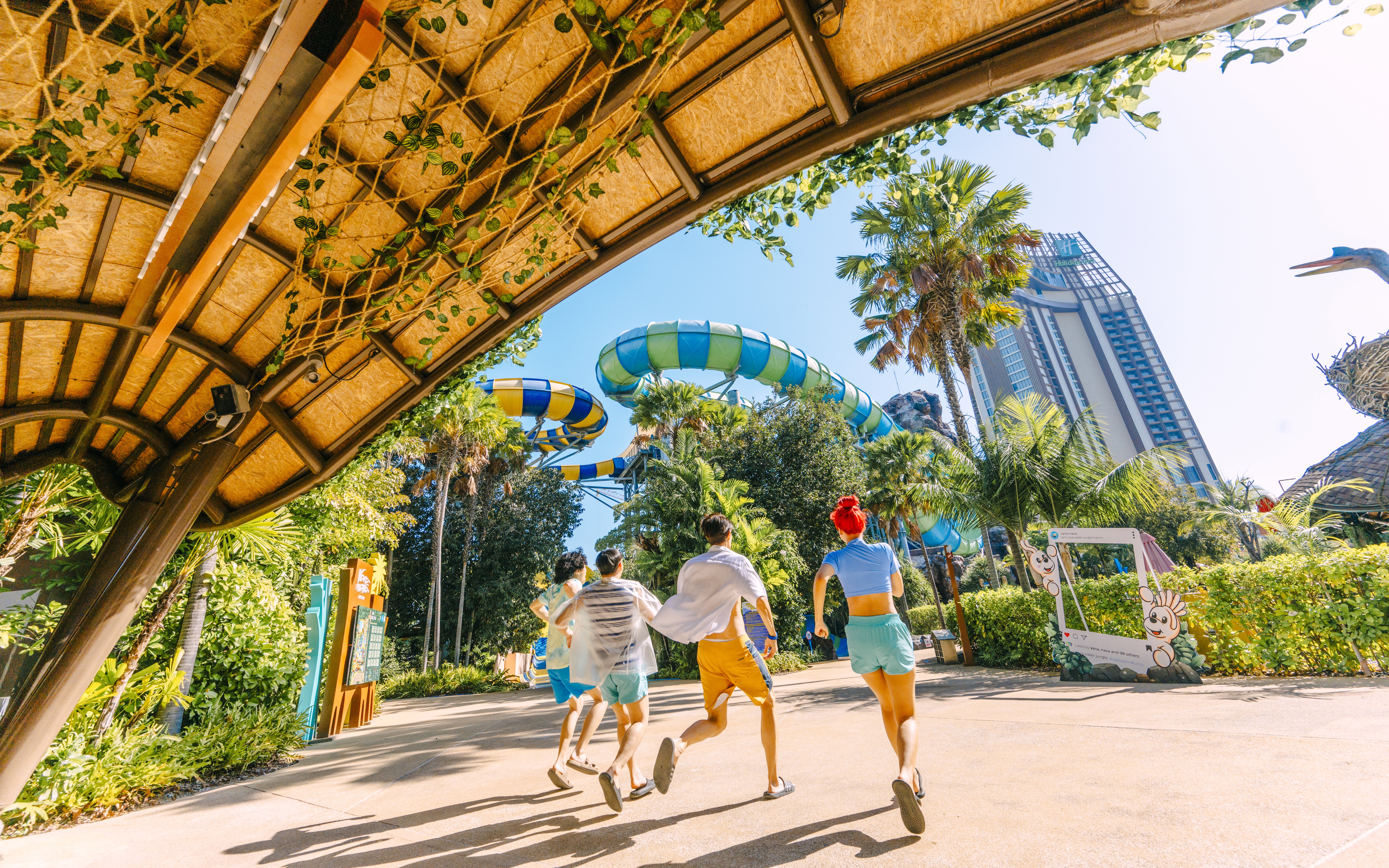 Visitors running towards water slides at Vana Nava Water Jungle, Hua Hin, surrounded by lush greenery.