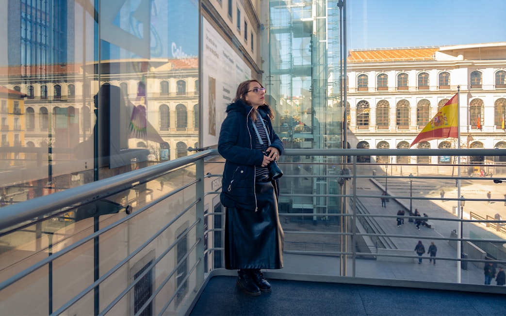 Woman observing art at Reina Sofia Museum, Madrid, with Spanish flag visible outside.