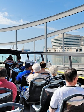 Tourists on a hop-on hop-off bus in Barcelona with waterfront view.