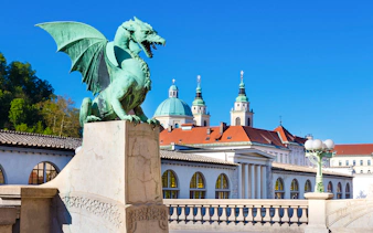 Dragon statue on Dragon Bridge with Ljubljana's skyline in the background, Slovenia.