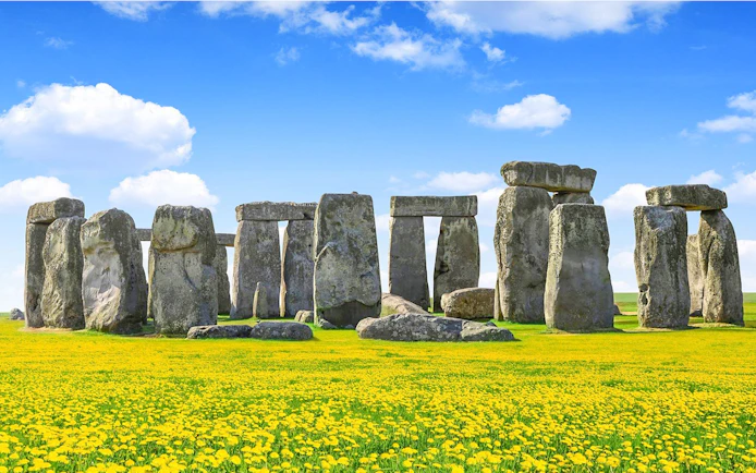 Stonehenge with blue sky and yellow flowers during daytime.