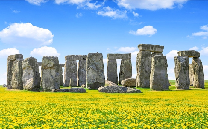 Stonehenge with blue sky and yellow flowers during daytime.
