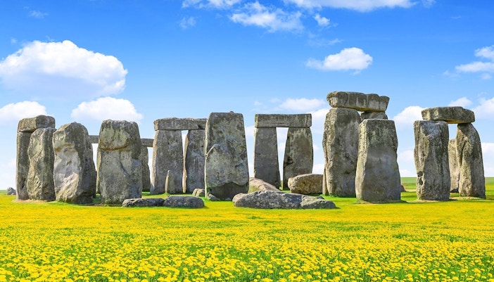 Stonehenge with blue sky and yellow flowers during daytime.