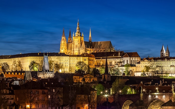 Prague Castle glowing at night with city lights in the background.