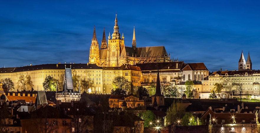 Prague Castle glowing at night with city lights in the background.