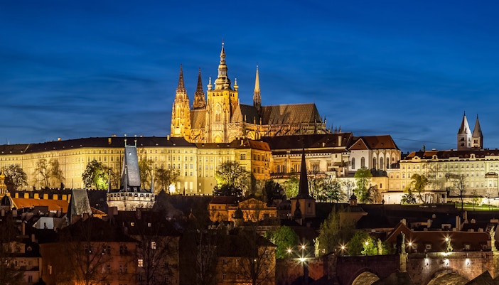 Prague Castle glowing at night with city lights in the background.