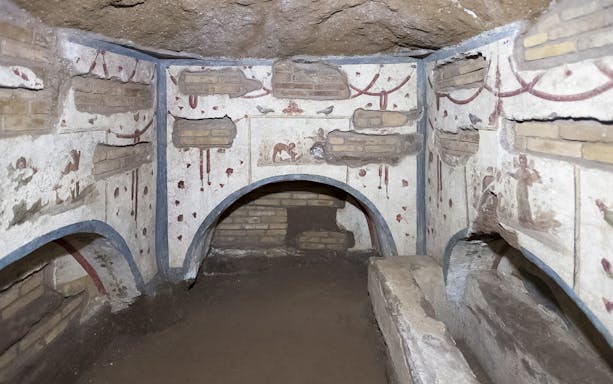 Ancient Roman catacombs with frescoes and arched niches in Rome.