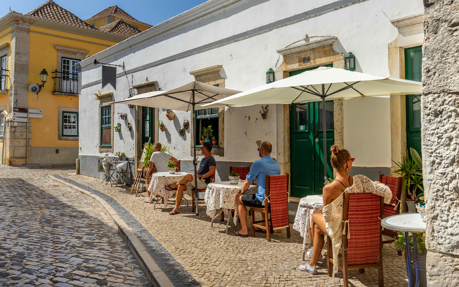 Outdoor café in Sintra with people seated under umbrellas on a cobblestone street.