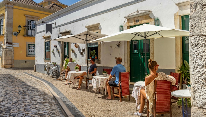 Outdoor café in Sintra with people seated under umbrellas on a cobblestone street.