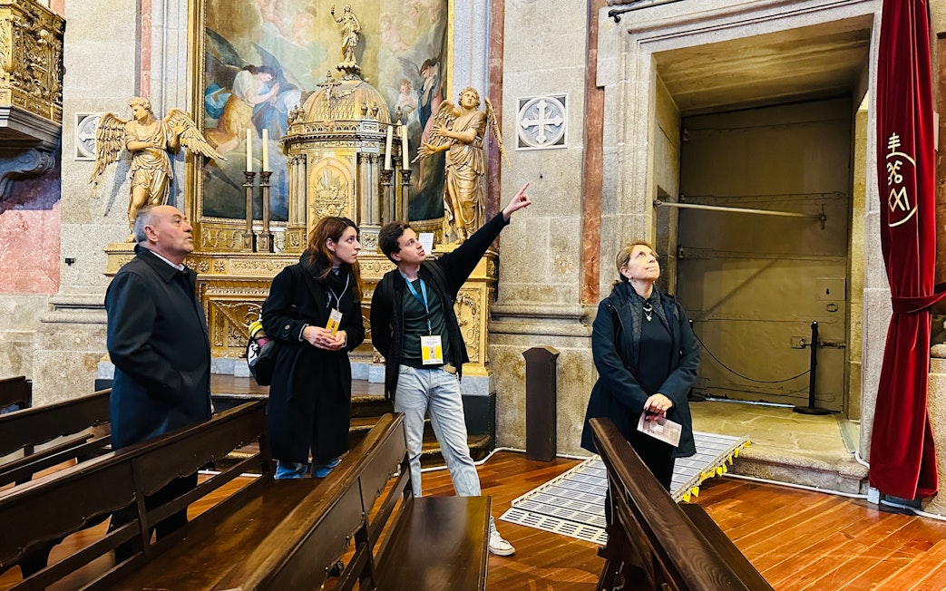 Visitors on a guided tour inside Clérigos Church, Porto, observing ornate altar and artwork.