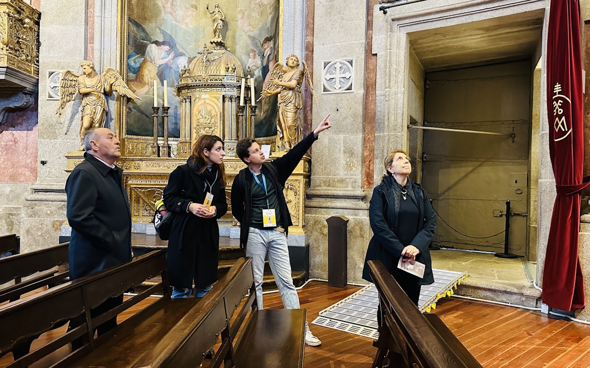 Visitors on a guided tour inside Clérigos Church, Porto, observing ornate altar and artwork.