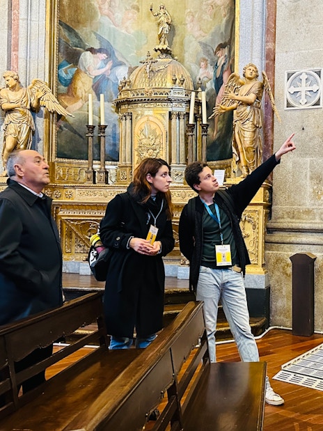 Visitors on a guided tour inside Clérigos Church, Porto, observing ornate altar and artwork.