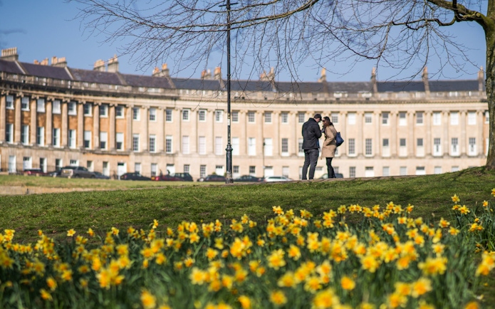 Royal Crescent in Bath with visitors on Bridgerton tour, daffodils in foreground.