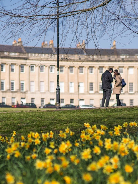 Royal Crescent in Bath with visitors on Bridgerton tour, daffodils in foreground.