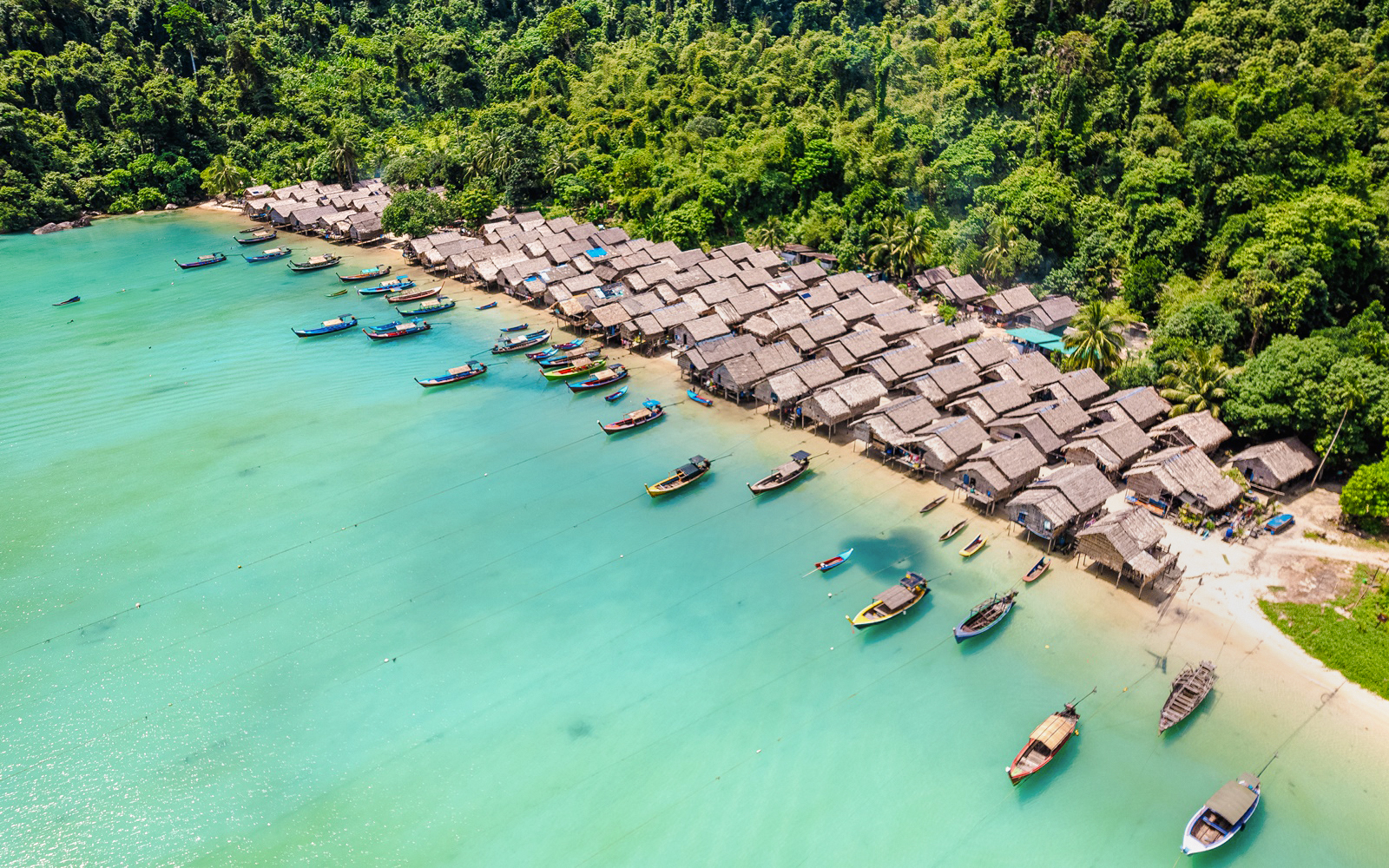 Boats lined up on the shore of Moken village, surrounded by lush greenery.