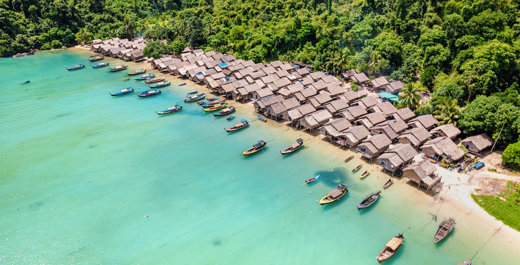 Boats lined up on the shore of Moken village, surrounded by lush greenery.