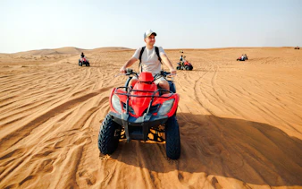 Man riding a red quad bike in the desert near Doha.
