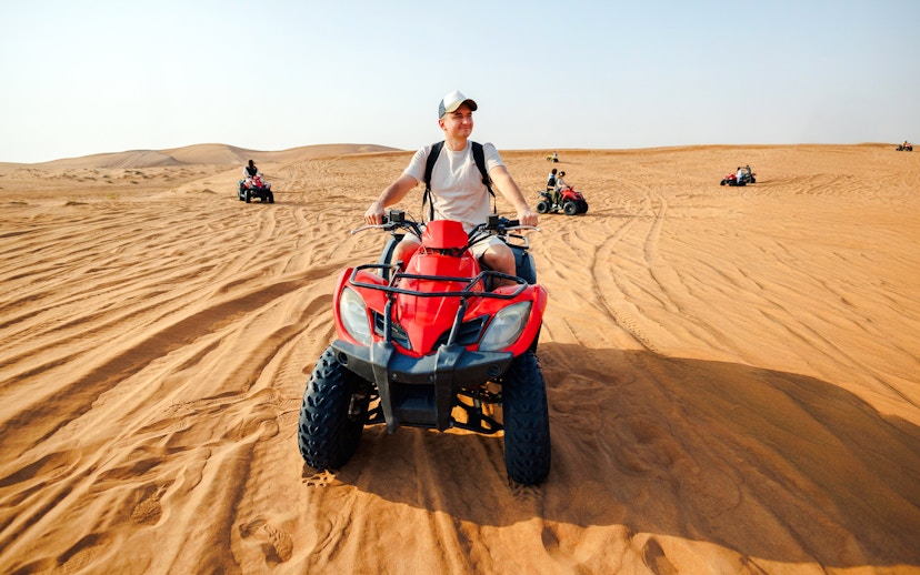 Man riding a red quad bike in the desert near Doha.