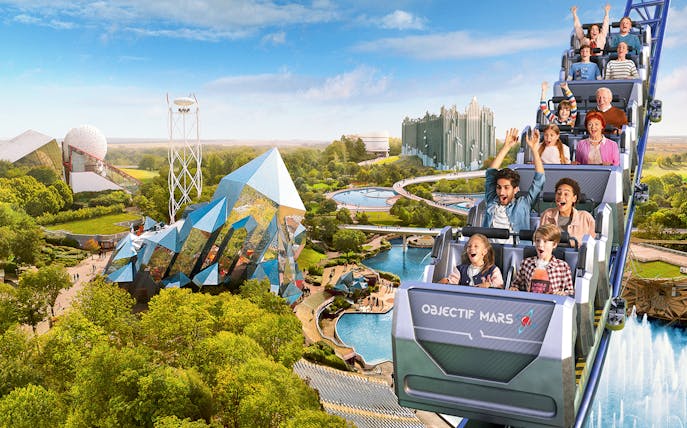 Roller coaster at Futuroscope with excited riders and futuristic architecture in the background.