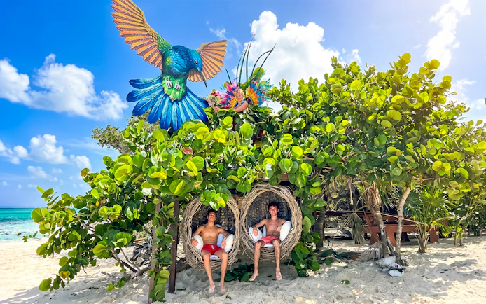 People relaxing in nest chairs under lush greenery on Rose Island beach, Bahamas.