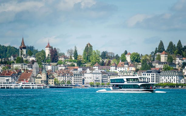 Catamaran cruising on Lake Lucerne with historic cityscape in the background.